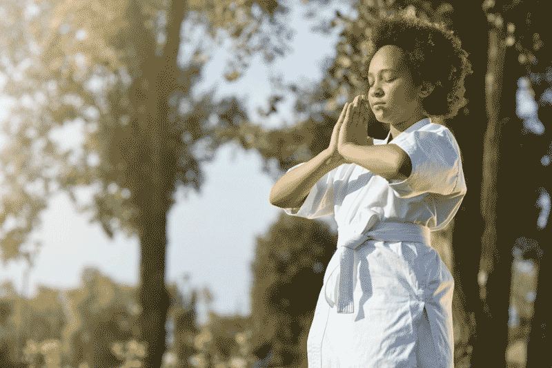 Foto de mulher negra de quimono branco meditando ao ar livre. A cultura japonesa tem muitos fãs no Brasil.