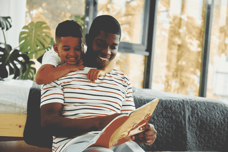 Foto de pai e filho lendo juntos. Atividades em família e lúdicas ajudam em como ensinar a ler.
