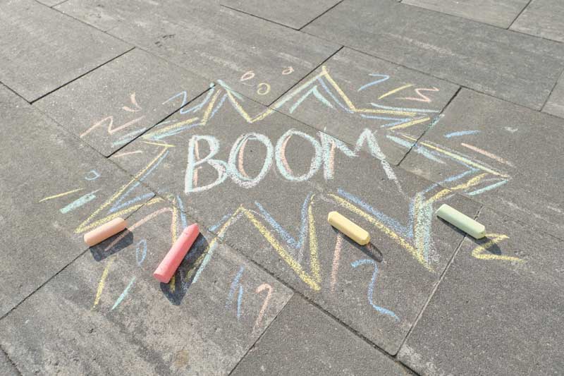 Foto da palavra BOOM escrita no chão com giz colorido. A onomatopeia é uma figura de linguagem baseada em sons.