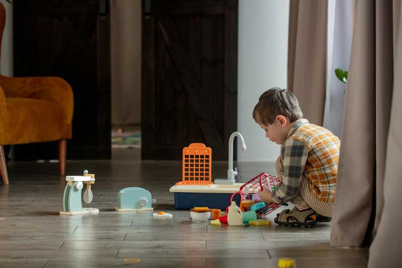 Foto de menino com vários brinquedos espalhados pelo chão. Guardá-los depois de brincar estimula a autonomia infantil.