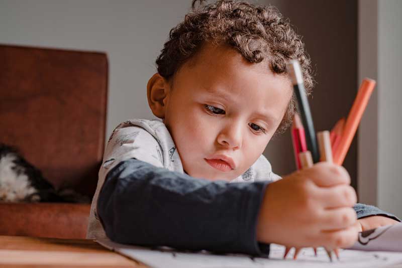 Foto de menino segurando vários lápis de cor sobre o papel. A escola tem papel fundamental na autonomia infantil.