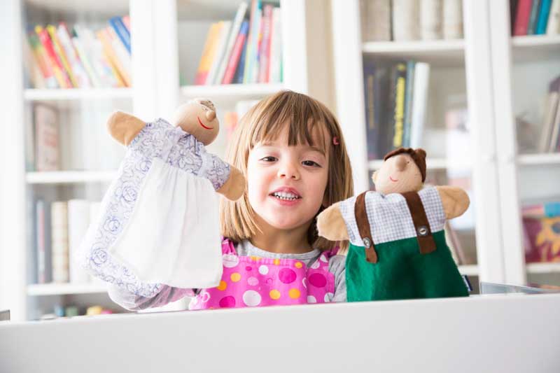 Foto de menina atrás de uma mesa com um fantoche em cada mão. Muitas ideias de atividades para educação infantil podem ser feitas em casa ou na escola.