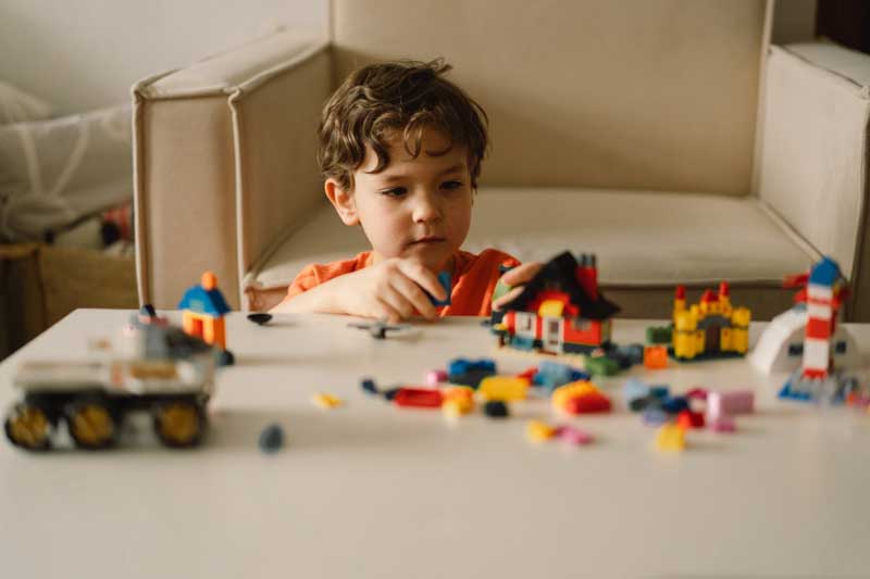 Foto de menino em casa brincando com blocos de montar. As atividades para educação infantil também podem ser feitas em casa com os pais.