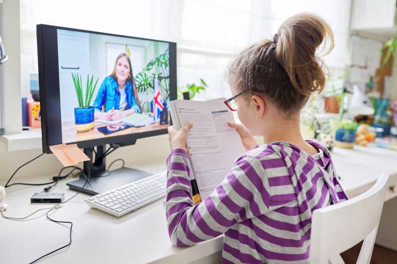 Foto de menina estudando inglês diante do computador. A educação bilíngue traz muitas vantagens.