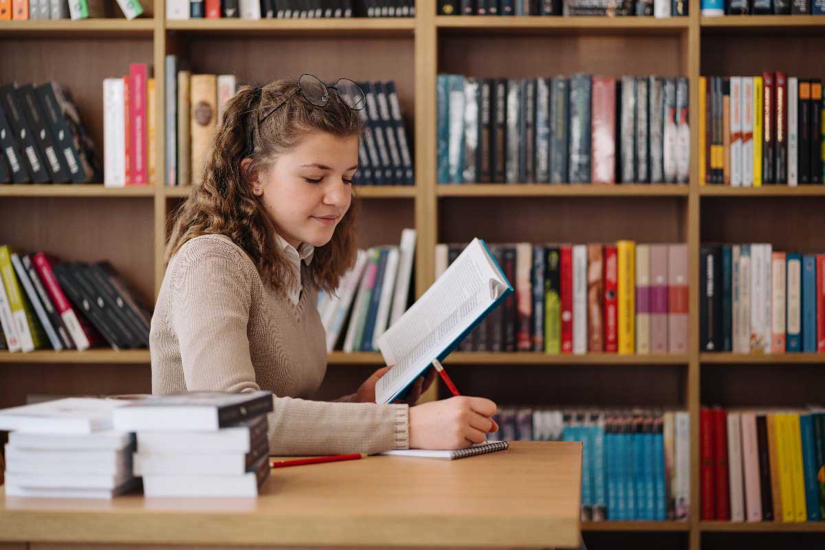 Foto de aluna estudando em biblioteca. Entender como estudar para prova exige bastante esforço e foco.