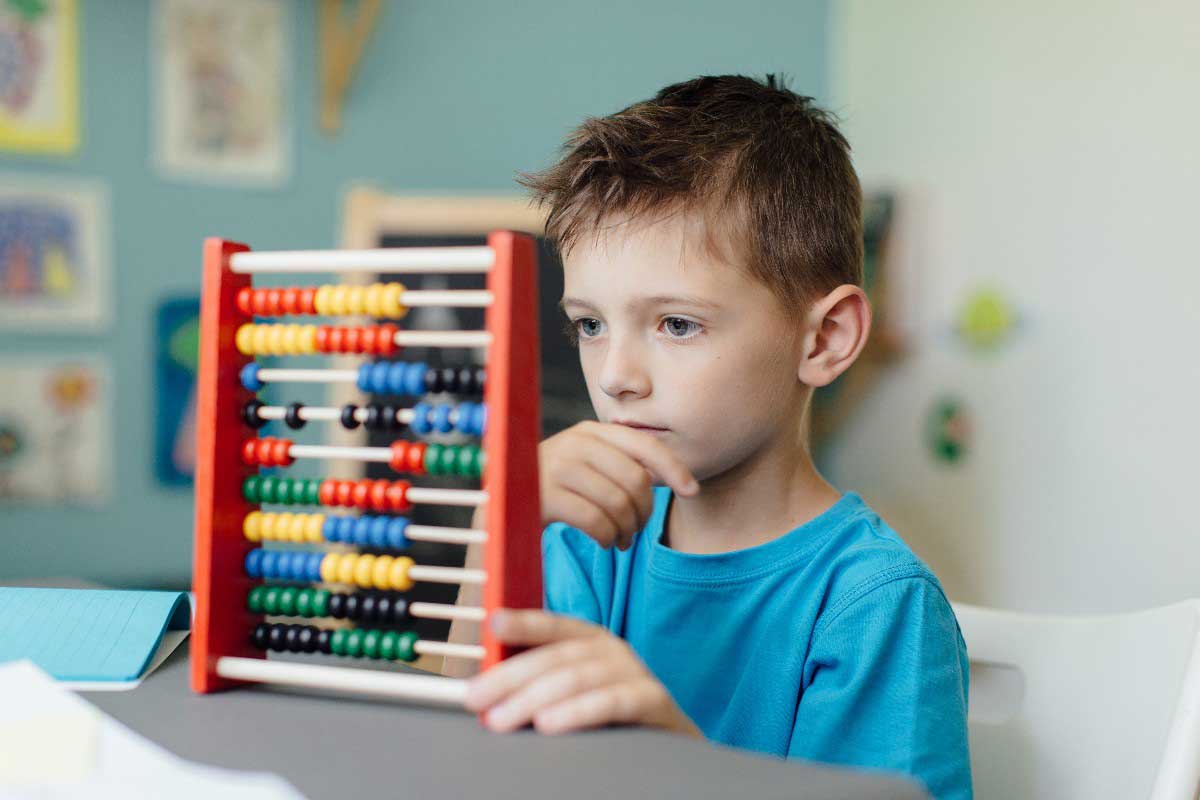 Foto de menino concentrado observando um ábaco. O método de ensino individual estimula o autodidatismo.