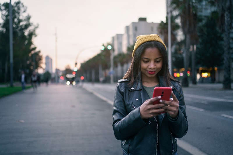 Foto de jovem menina usando jaqueta de couro, touca e enviando mensagem no celular. As abreviações e gírias em inglês são muito usadas na internet e em mensagens.