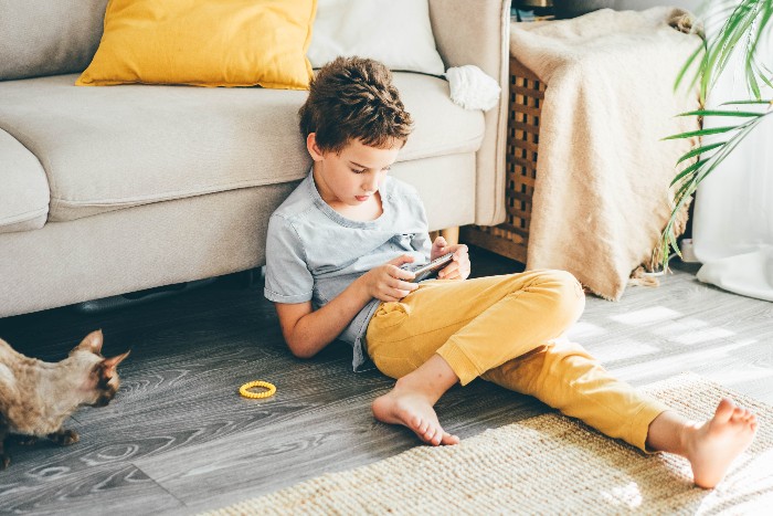  Foto de criança no celular sentada do chão, atenta ao aparelho.