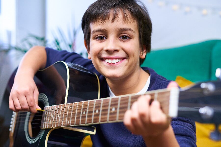 Foto de menino sorridente tocando violão.