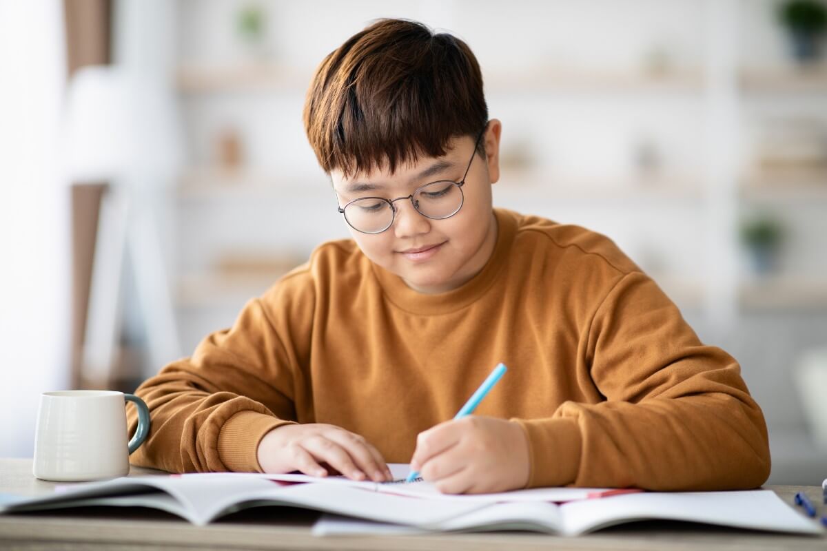 Foto de jovem com traços asiáticos praticando uso de vírgula em um caderno.