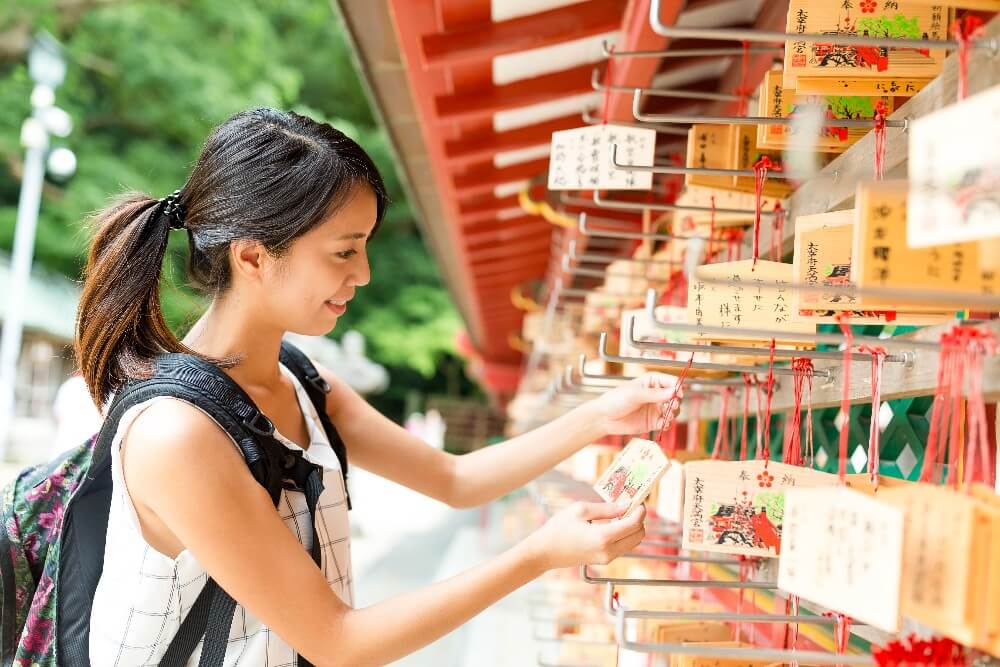 Foto de mulher oriental pendurando desejos de ano novo em um templo japonês.