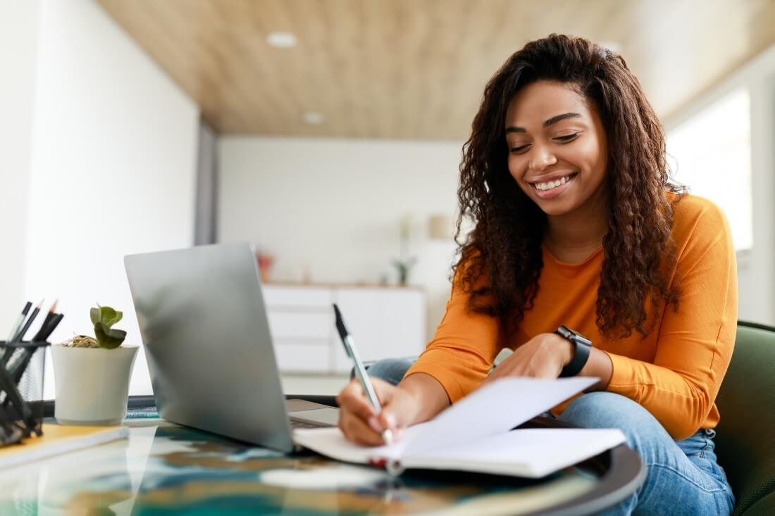 Foto de jovem mulher negra sorridente estudando concordância verbal e nominal.