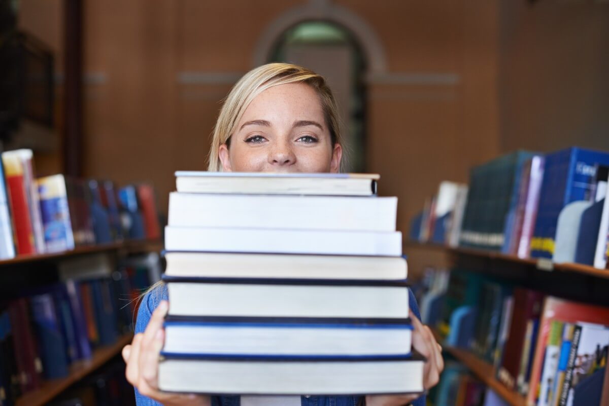 Foto de jovem loira segurando pilha de livros para estudar para o vestibular.