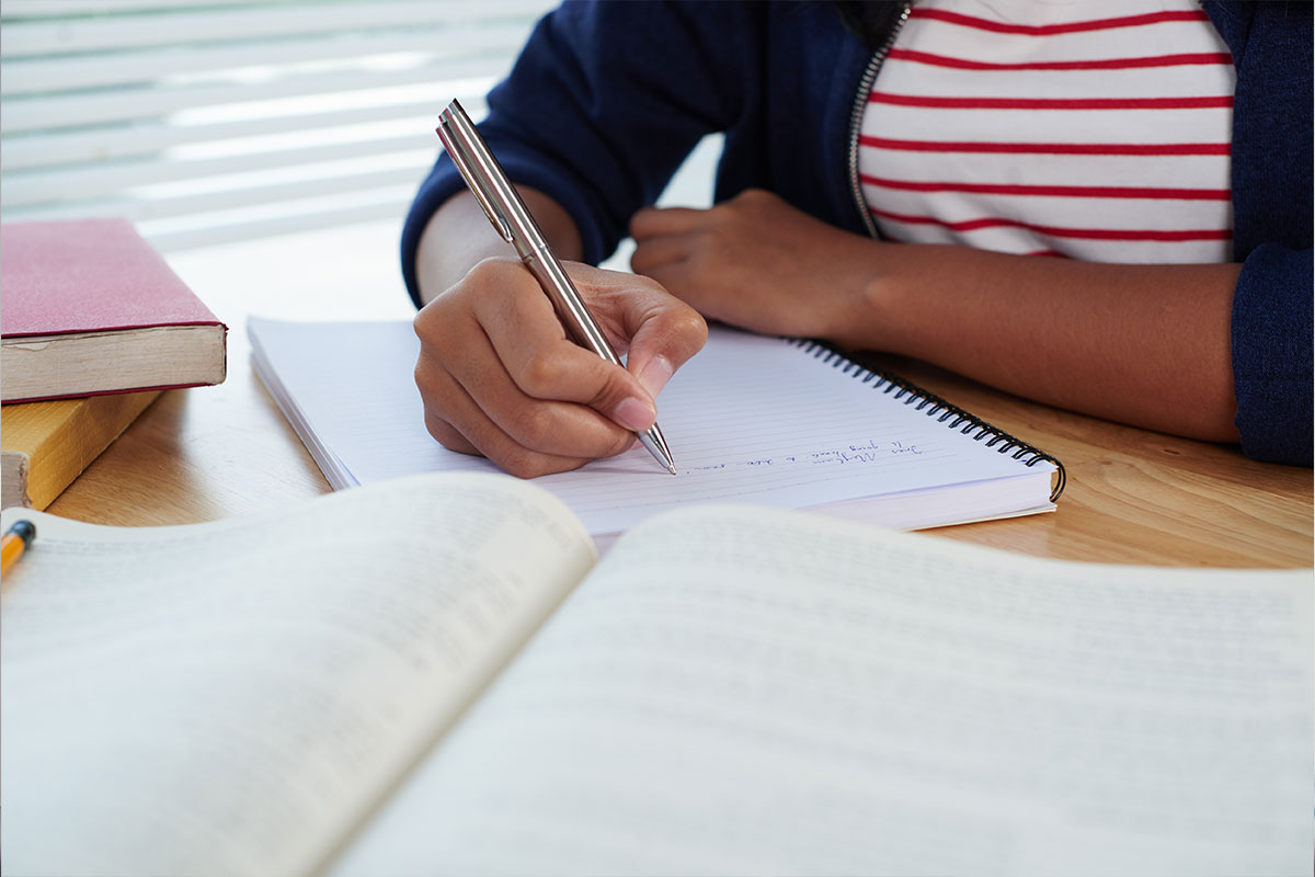 Foto de mãos de uma jovem escrevendo à caneta em um caderno.