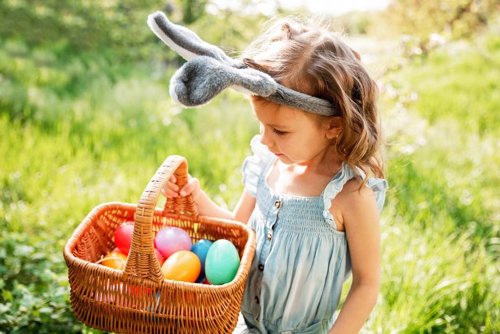 Menina segurando um cesto com ovos coloridos.