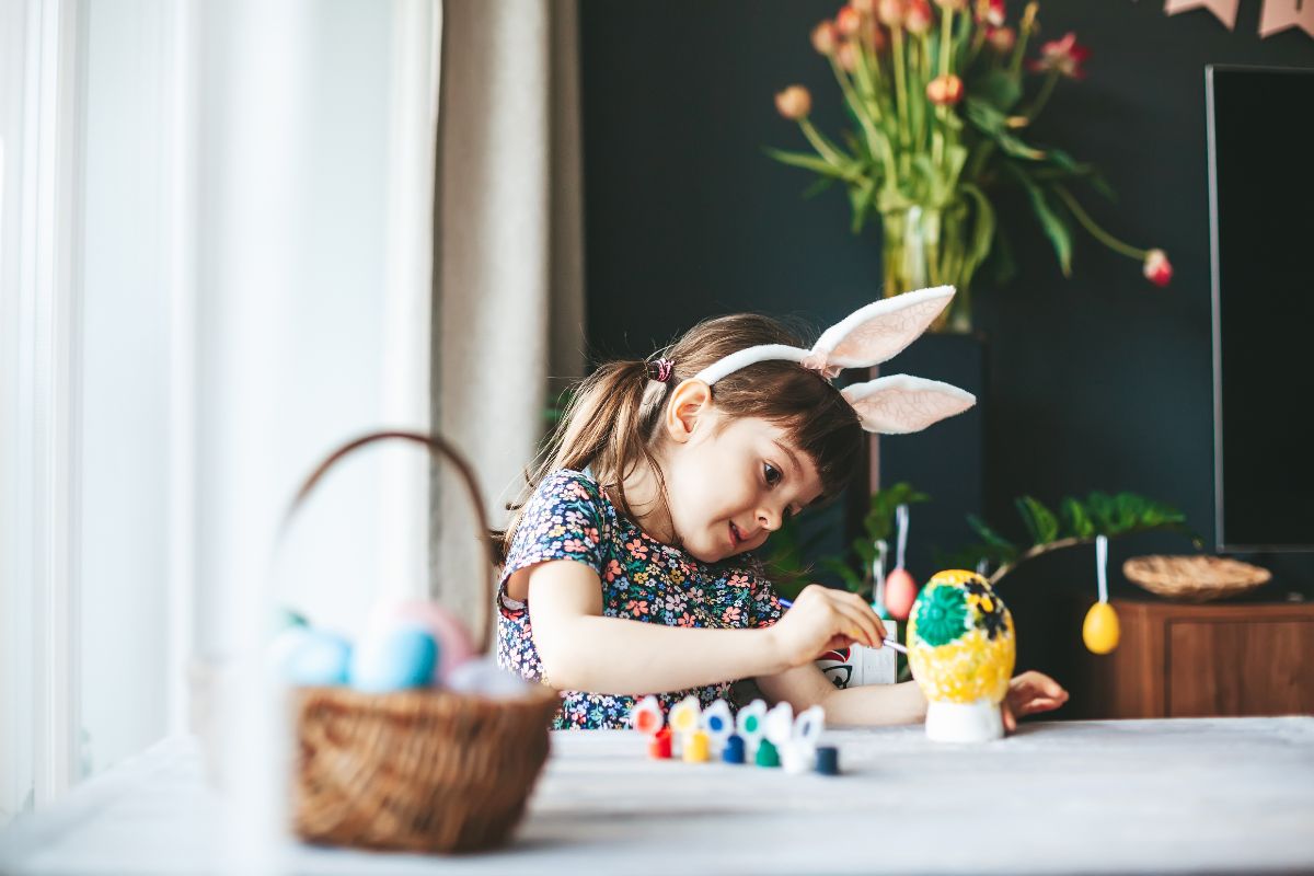 Menina com orelhas de coelho pintando ovos para uma atividade de páscoa.