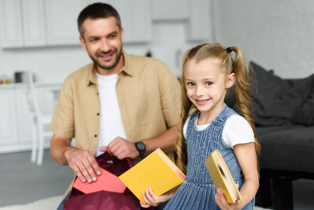 Pai ajudando sua filha a montar a sua mochila para o primeiro dia de aula.