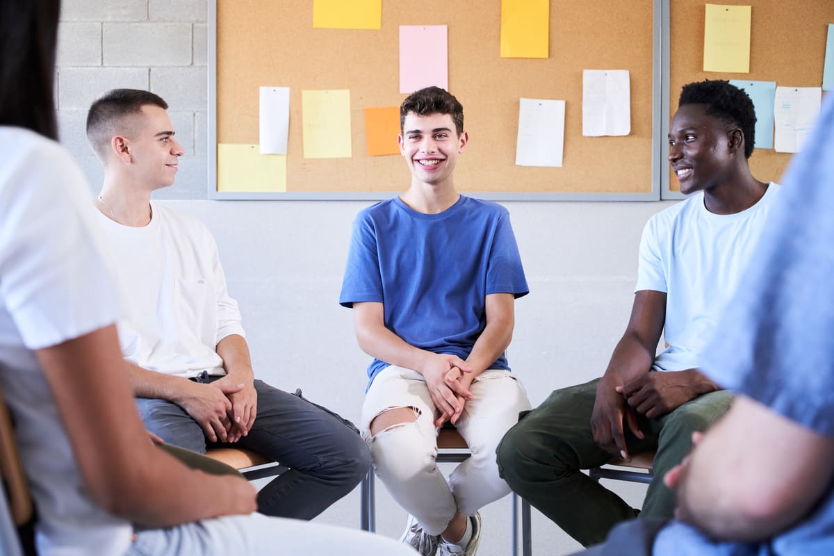 Jovens sorridentes sentados em cadeiras em círculo na sala de aula.