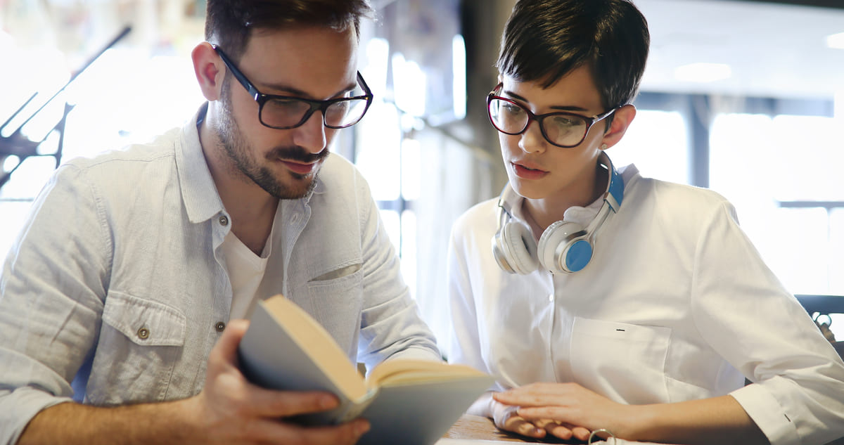 Dois jovens estudando com um livro.