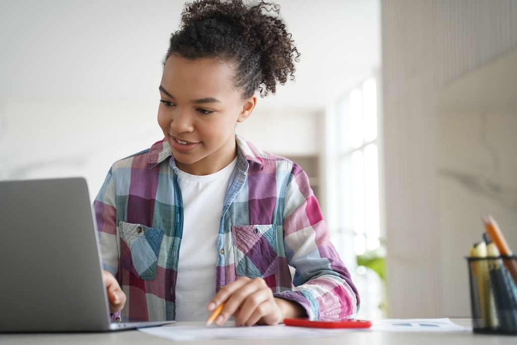 Menina estudando com lápis, papel e computador.