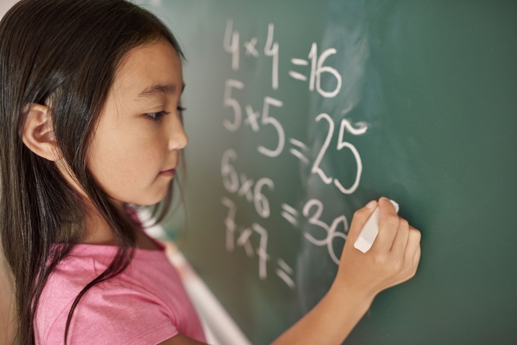 Foto de menina resolvendo exercícios de matemática em um quadro-negro
