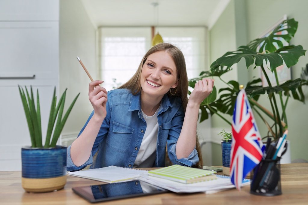 Menina sorridente estudando inglês em frente à bandeira do Reino Unido.