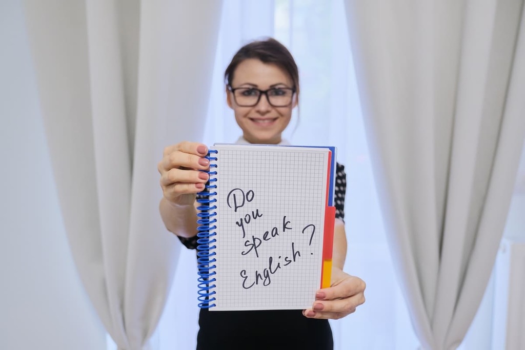 Mulher sorridente segurando um caderno escrito "do you speak english?"