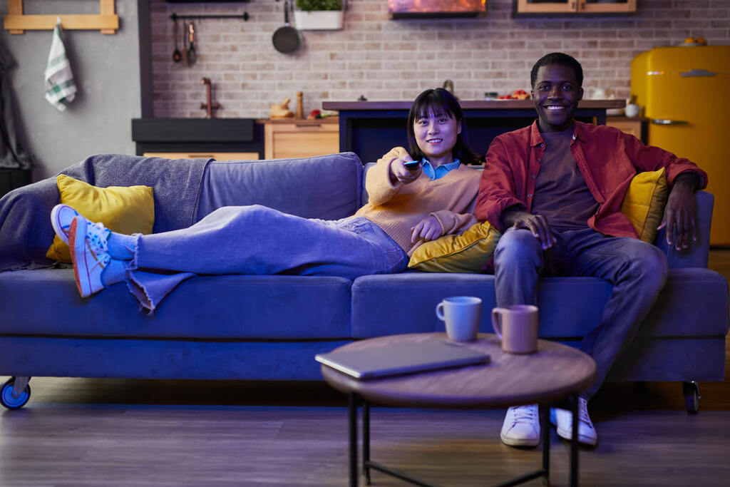 Homem e mulher jovens no sofá vendo televisão.