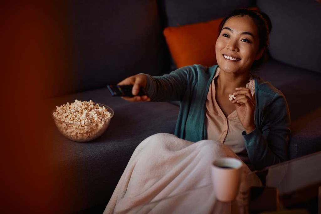 Mulher asiática assistindo filmes comendo pipoca.