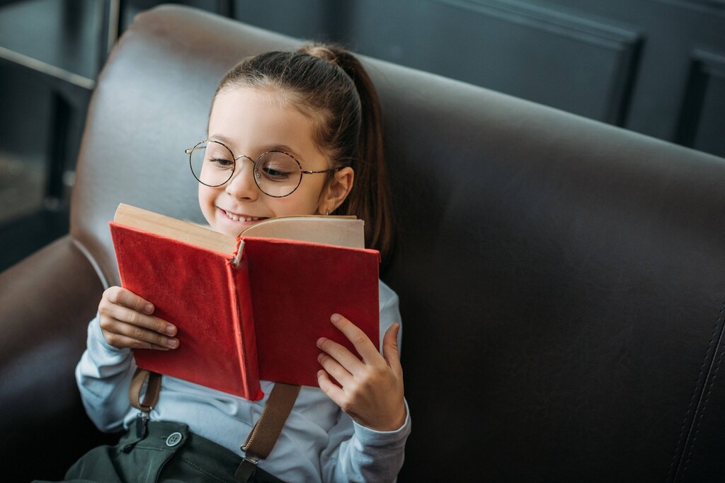 Menina sorrindo e lendo um livro de capa vermelha