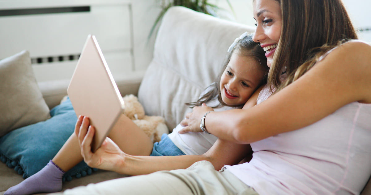 Mãe feliz com sua filha usando tablet para fazer leitura digital.
