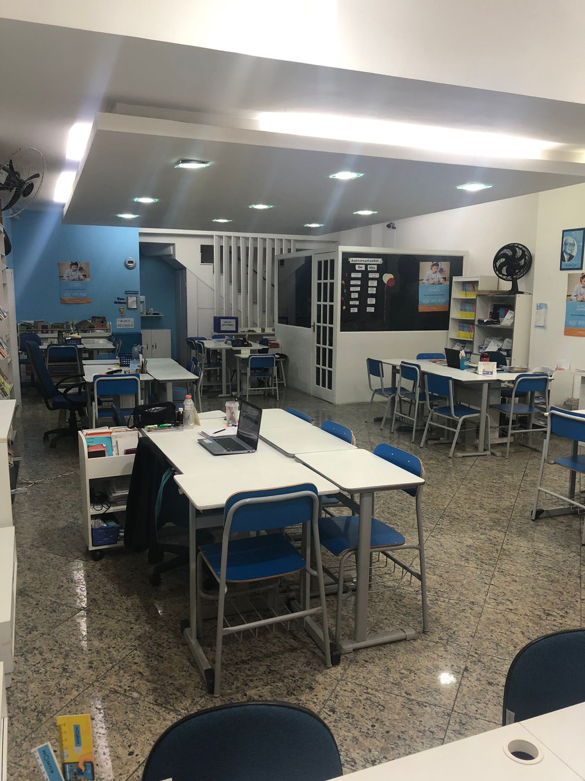 Interior da sala de aula da unidade Kumon Teresópolis-Alto, com mesas e cadeiras azuis organizadas para os alunos, e um quadro branco ao fundo.