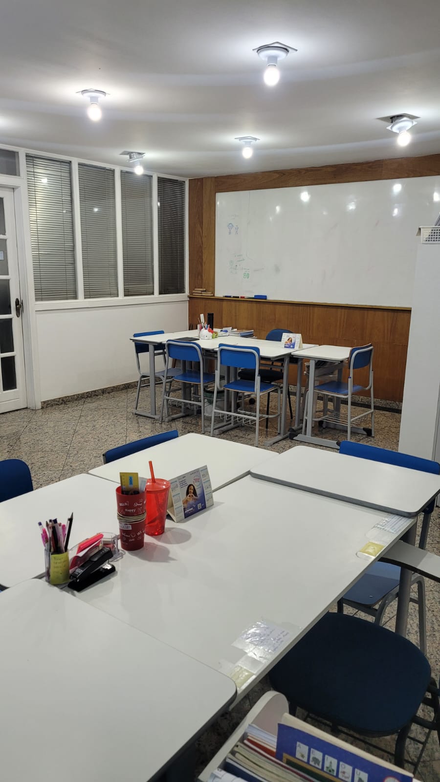 Interior da sala de aula da unidade Kumon Teresópolis-Alto, com mesas e cadeiras azuis organizadas para os alunos, e um quadro branco ao fundo.