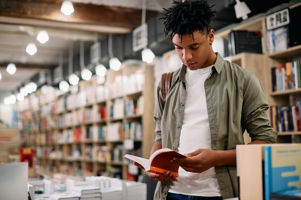 Estudante lendo um livro em inglês em uma biblioteca.