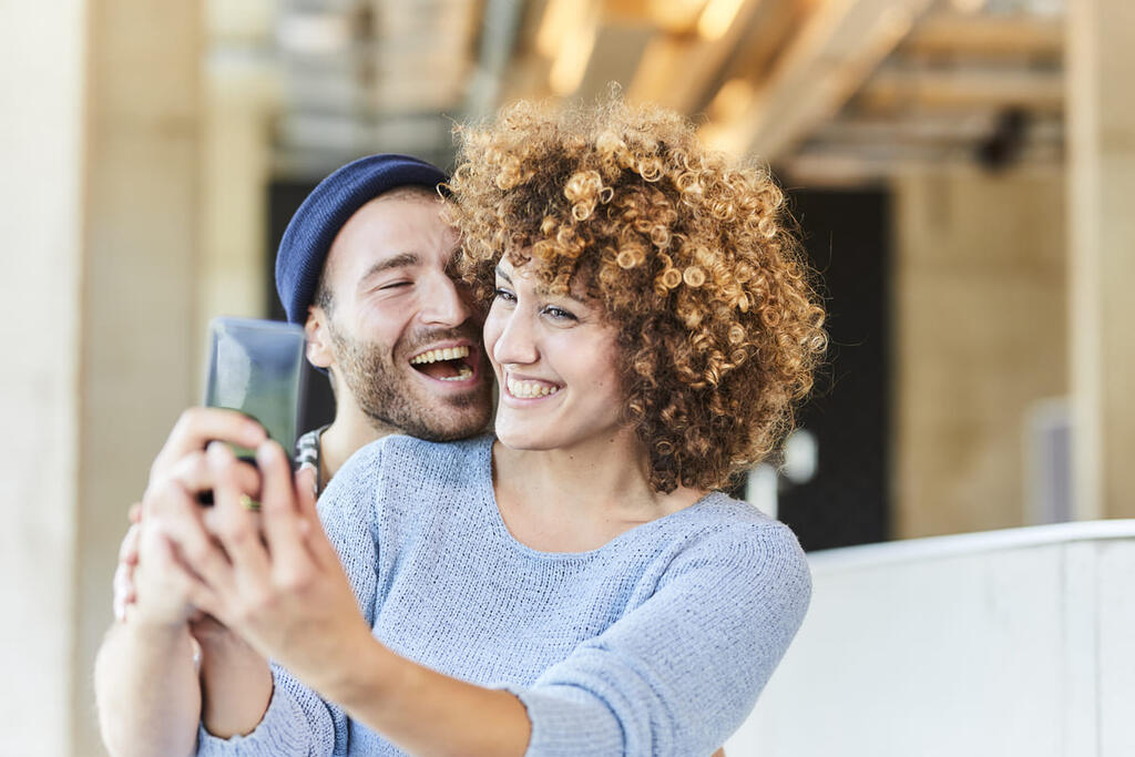 Casal rindo tirando uma selfie.