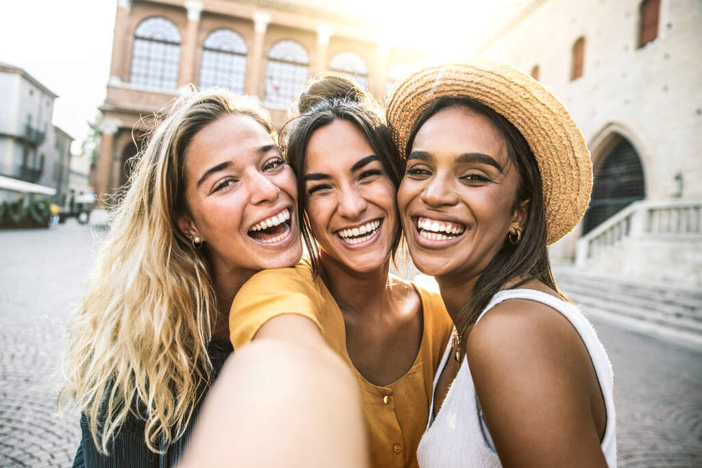 Três jovens mulheres tirando selfie na rua da cidade.