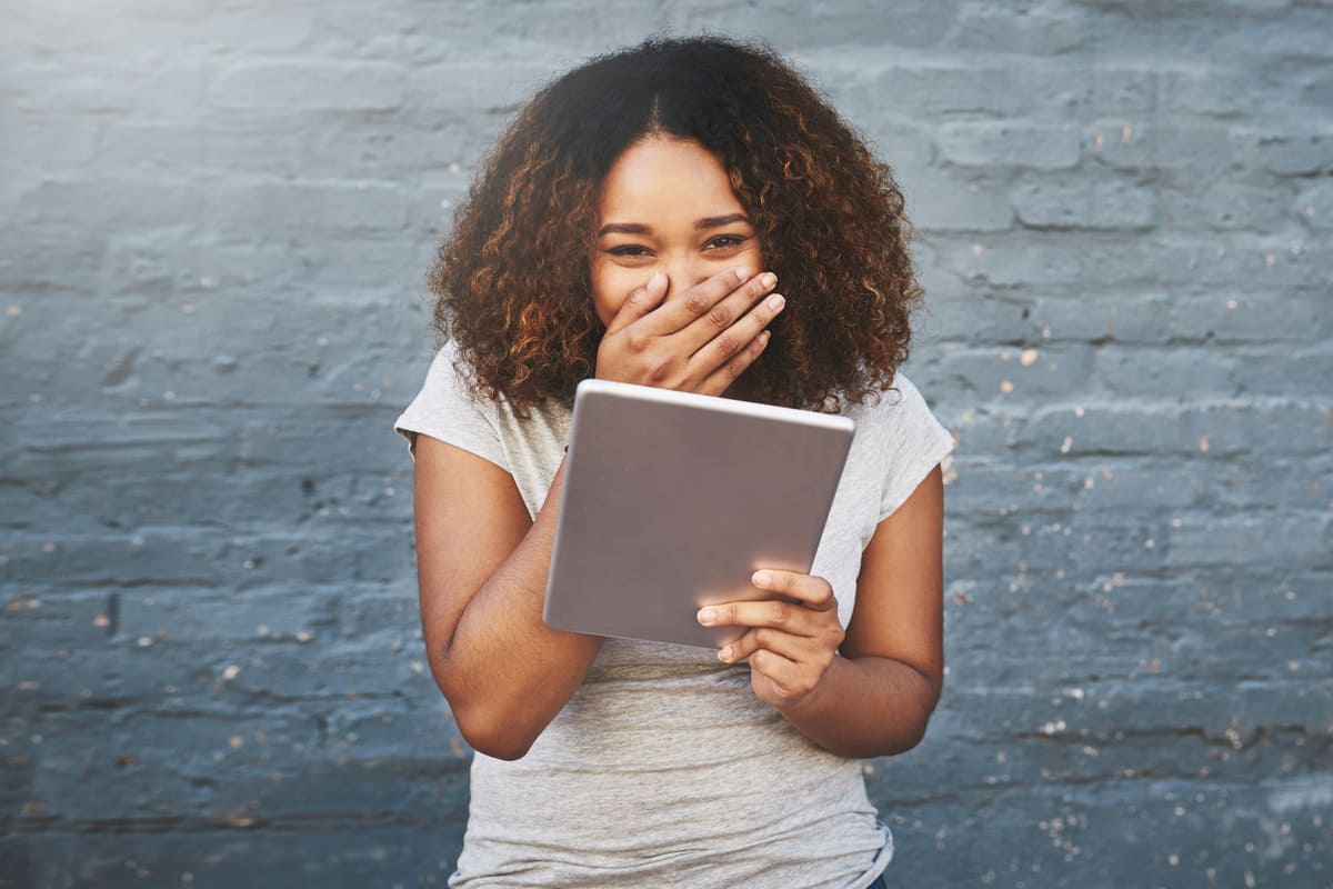 Mulher rindo com tablet na mão.