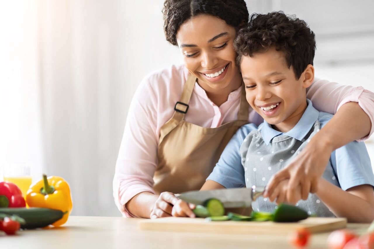 Mãe ensinando filho a cortar vegetais na cozinha.