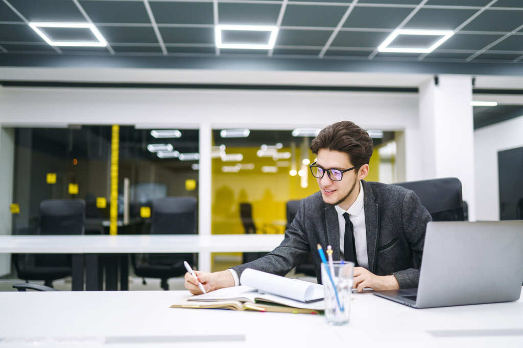 Jovem gerente de escritório trabalhando com papéis e computador.