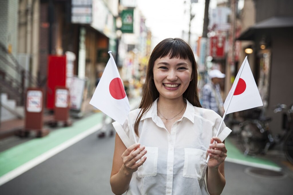 Mulher japonesa sorridente em pé em uma rua, segurando a pequena bandeira japonesa.