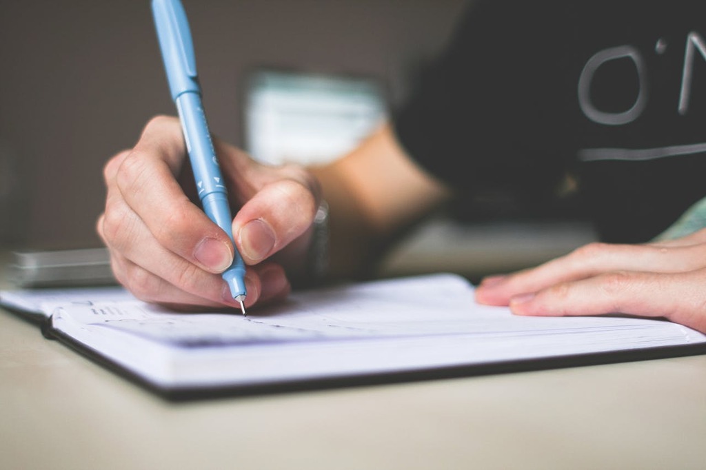 pessoa escrevendo meses do ano em inglês no caderno com caneta azul