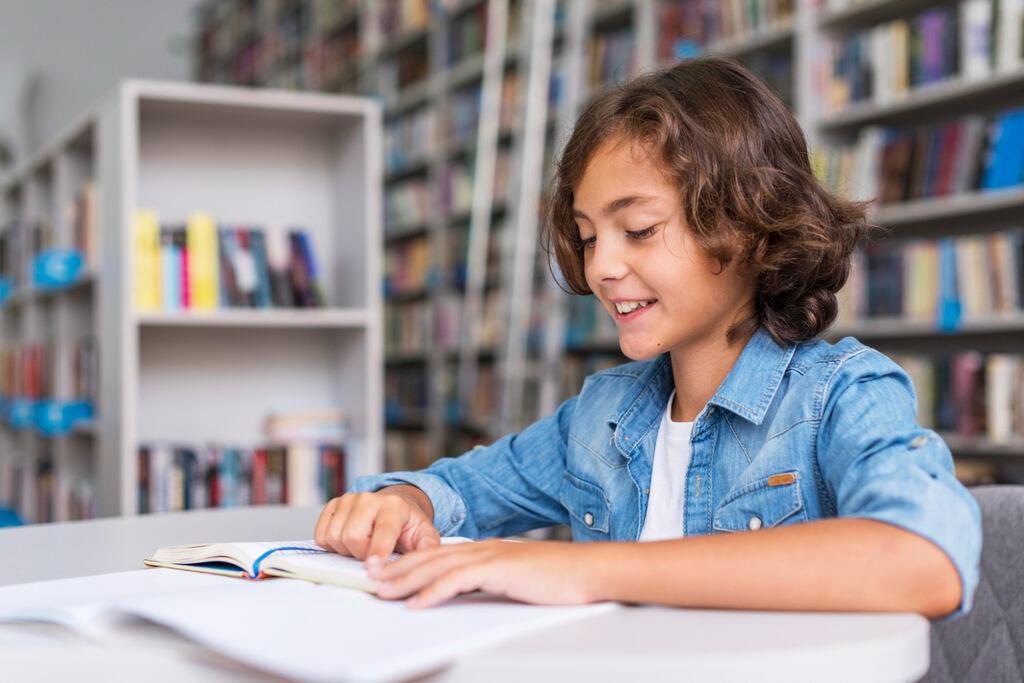 criança lendo livro em biblioteca depois de aprender a função da língua portuguesa