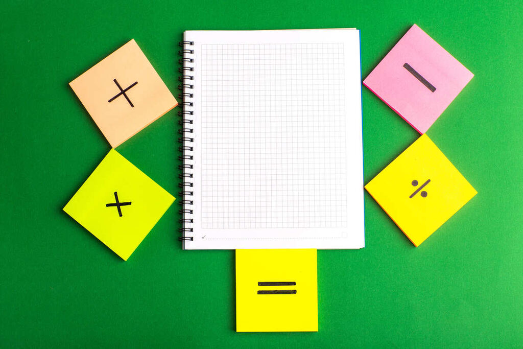 Caderno de matemática e papeis com sinais de operações matemáticas