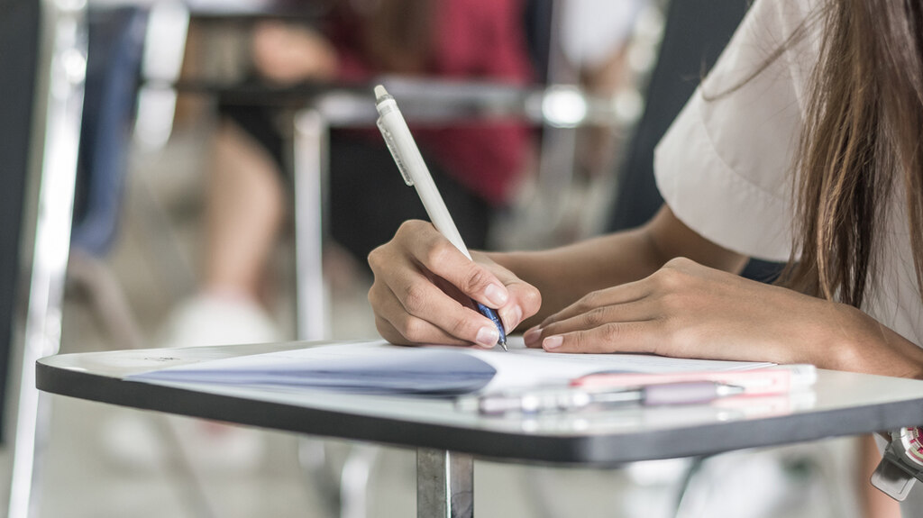 Estudante escrevendo em folha oficial de exame, em exemplo prático de como escrever uma redação em vestibular ou concurso.
