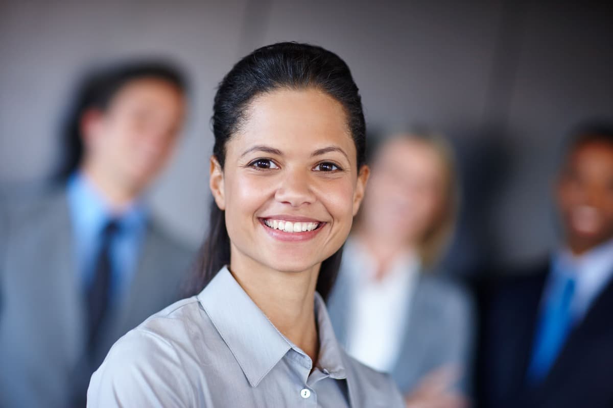 Empreendedora sorridente enquanto colegas sorriem ao fundo, desfocados.