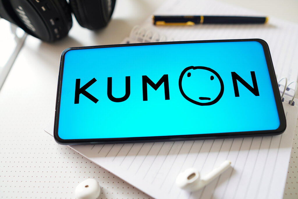 Logo do Kumon em tela de celular, ao lado de caneta e caderno, representando material didático Kumon.