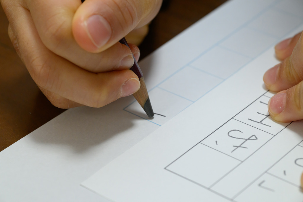 Mão de pessoa utilizando lápis para aprender a escrever kanjis japoneses para pedir comida em restaurante.