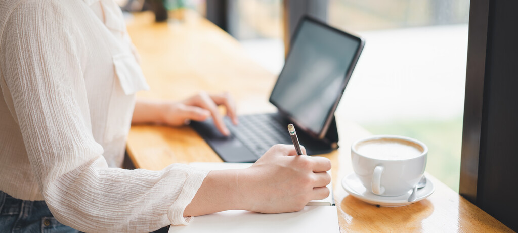 Mulher utilizando notebook e caderno para pesquisar qual a frase do gojo.