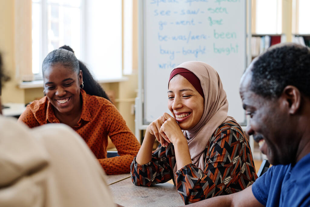 Quatro pessoas de nacionalidades diferentes sorrindo ao redor de mesa, estudando quando usar make or do.