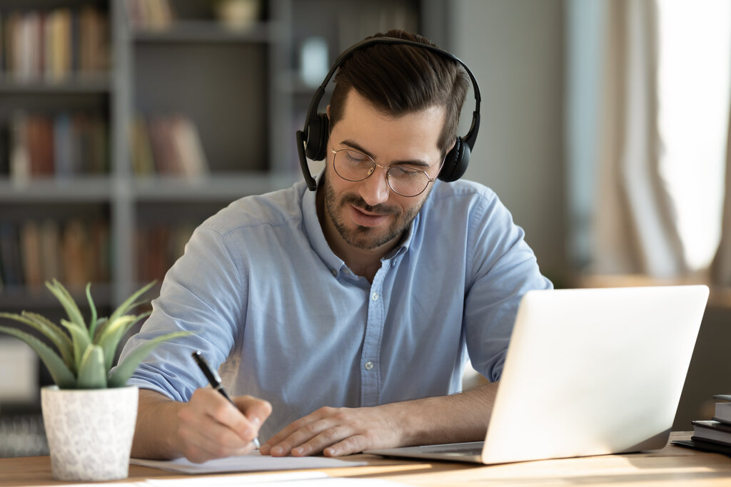 Homem de fones de ouvido utilizando notebook, papel e caneta para estudar quando usar do or make.